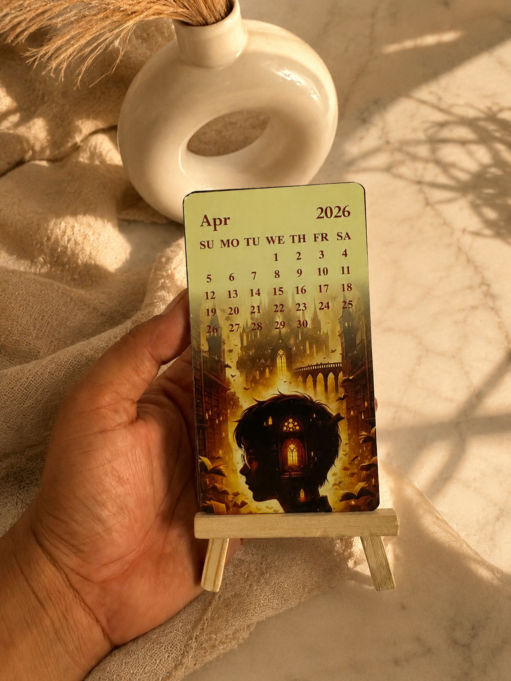 Hand holding a small calendar with a decorative design on a textured surface
